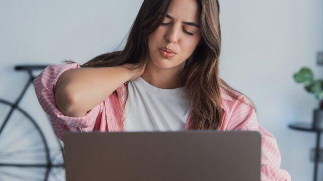 Donna seduta a un laptop si massaggia la nuca con disagio