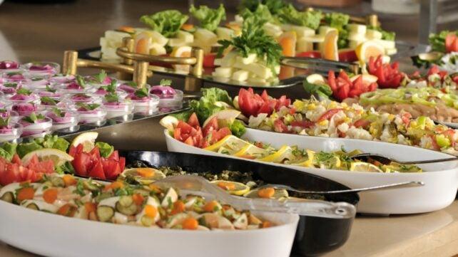 Buffet con vassoi di insalate, verdure, formaggi, uova e utensili da portata condivisi