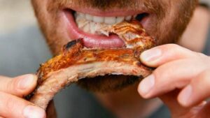 Primo piano di un uomo che mangia una costina alla griglia