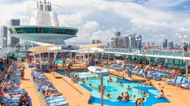 Passeggeri che si rilassano attorno a piscine affollate e lettini sul ponte di una nave da crociera