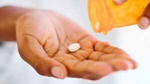 mano che tiene una pillola, con un'altra pillola che esce da un barattolo di prescrizione arancione