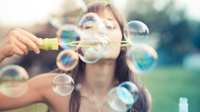 Una persona all'aperto che soffia bolle di sapone iridescenti attraverso un bastoncino per bolle.
