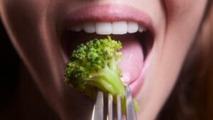Giovane donna che mangia broccoli