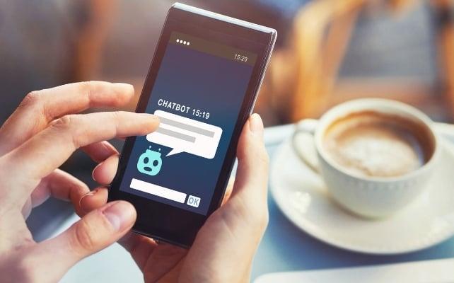 Persona che utilizza un chatbot su uno smartphone a un tavolo accanto a una tazza di caffè