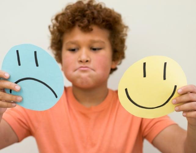 Un bambino che tiene in mano facce disegnate sorridenti e tristi