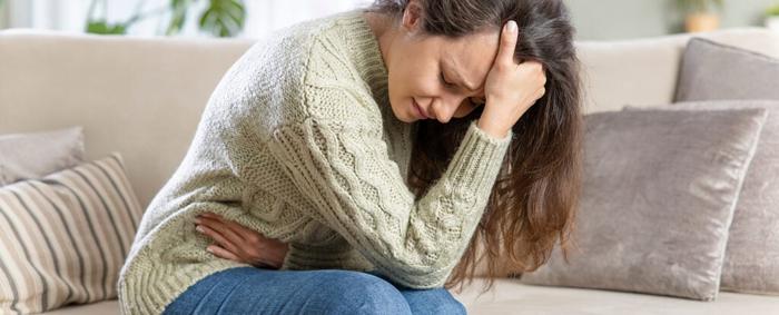 Una donna piegata in due dal dolore, che si tiene lo stomaco e culla la testa tra le mani.