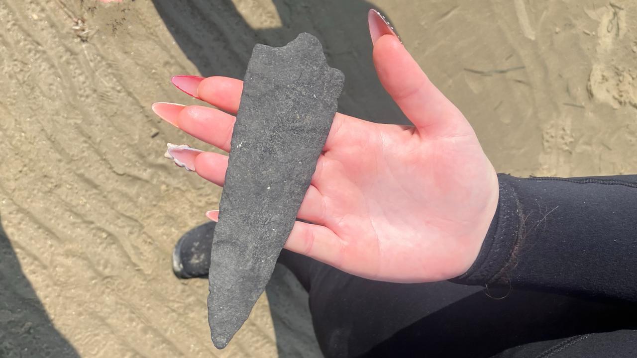 una persona dalla pelle chiara e con le unghie lunghe e curate tiene una punta di lancia di pietra sul palmo aperto