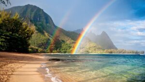 Un doppio arcobaleno sopra una spiaggia, con un versante montuoso sullo sfondo
