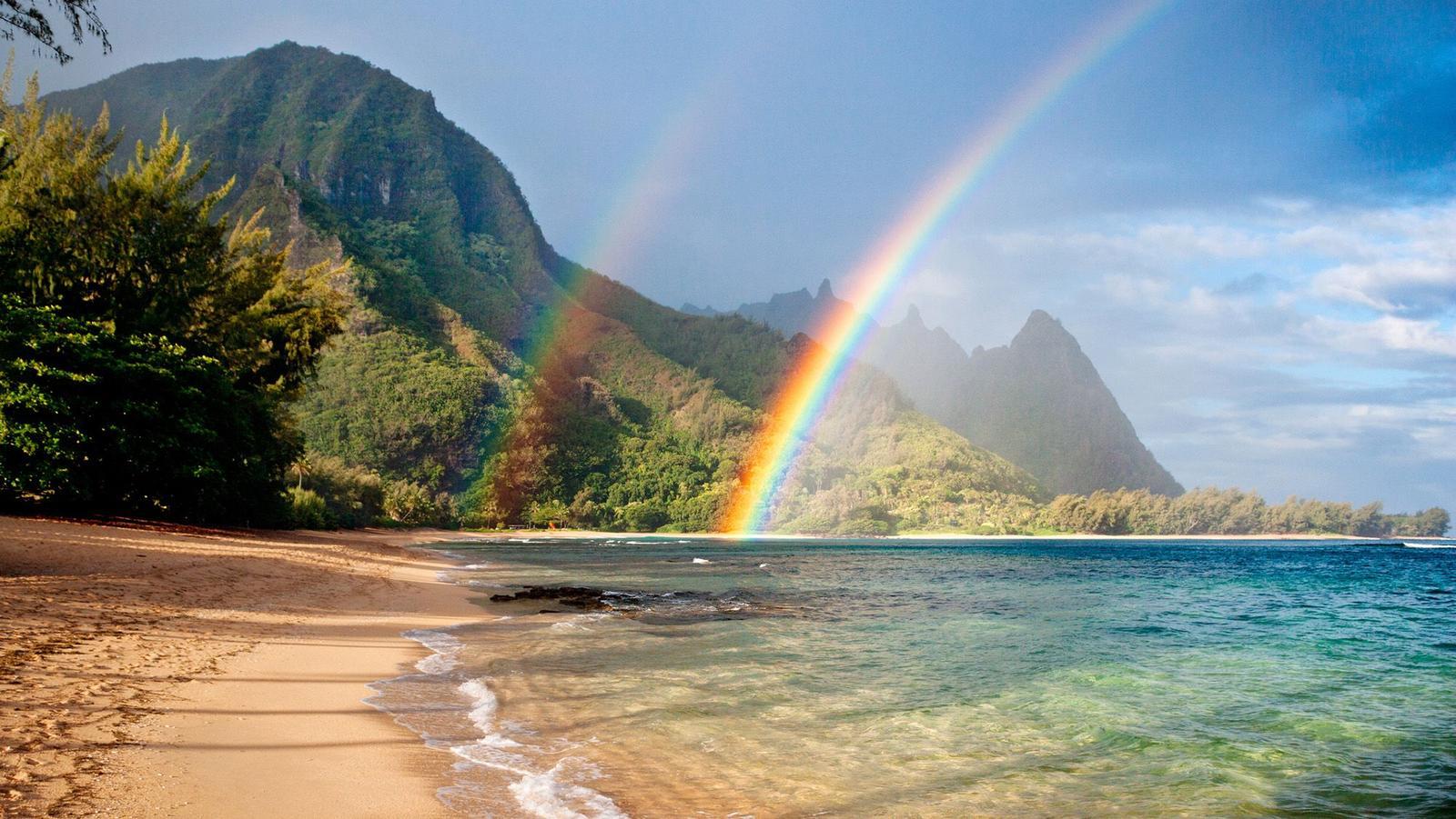 Un doppio arcobaleno sopra una spiaggia, con un versante montuoso sullo sfondo