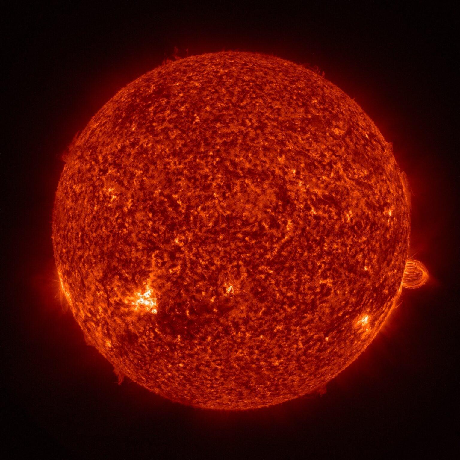 Archi di plasma arancione brillante si innalzano oltre il bordo del Sole su uno sfondo nero, in un’immagine ultravioletta a colori.