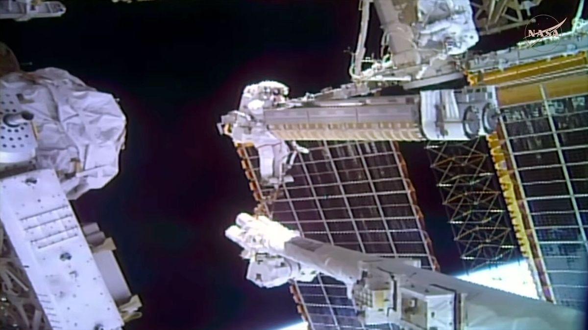 un astronauta in tuta spaziale regge un grosso carico mentre si trova all’estremità di un braccio robotico all’esterno di una stazione spaziale