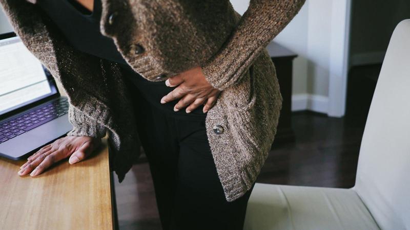 Una donna con una maglia nera e un maglione marrone si stringe l’addome